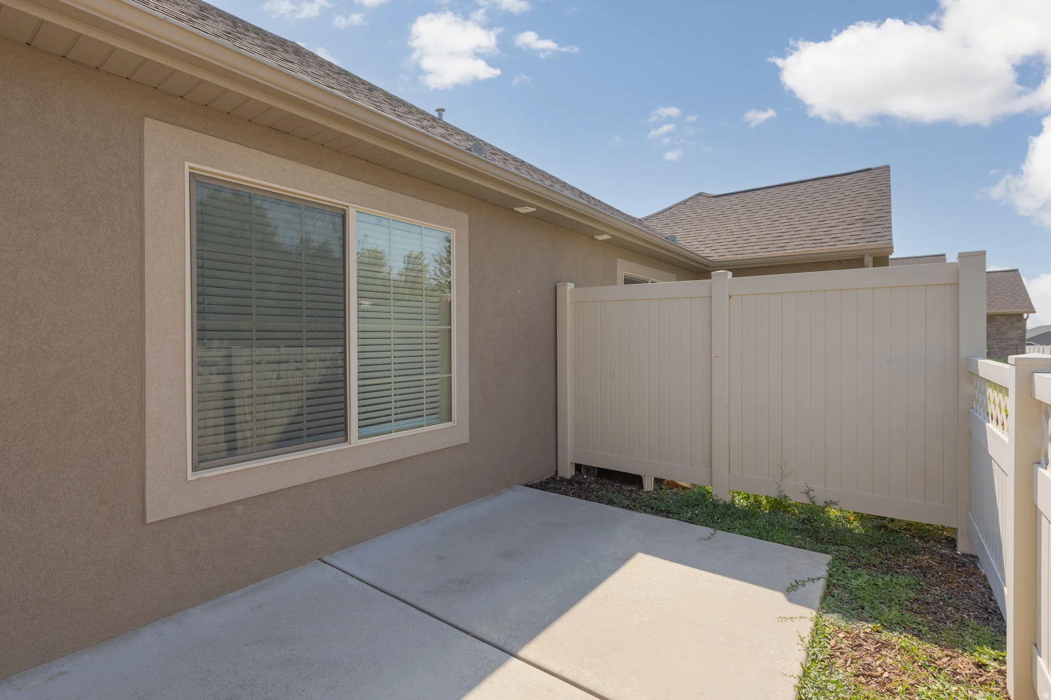 Stucco exterior with a single window featuring blinds, complemented by a concrete patio and a privacy fence