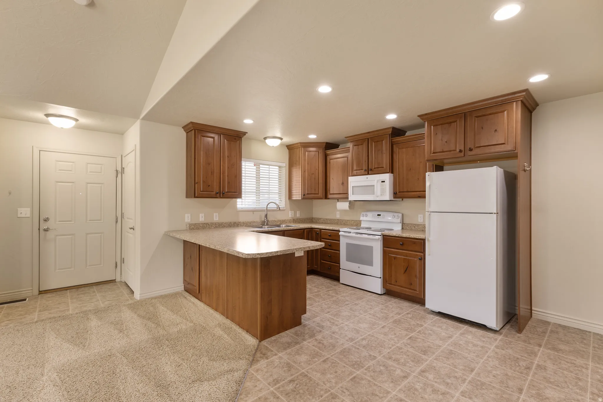 Kitchen featuring wood cabinetry, white appliances, L-shaped countertop, recessed lighting, and tile flooring