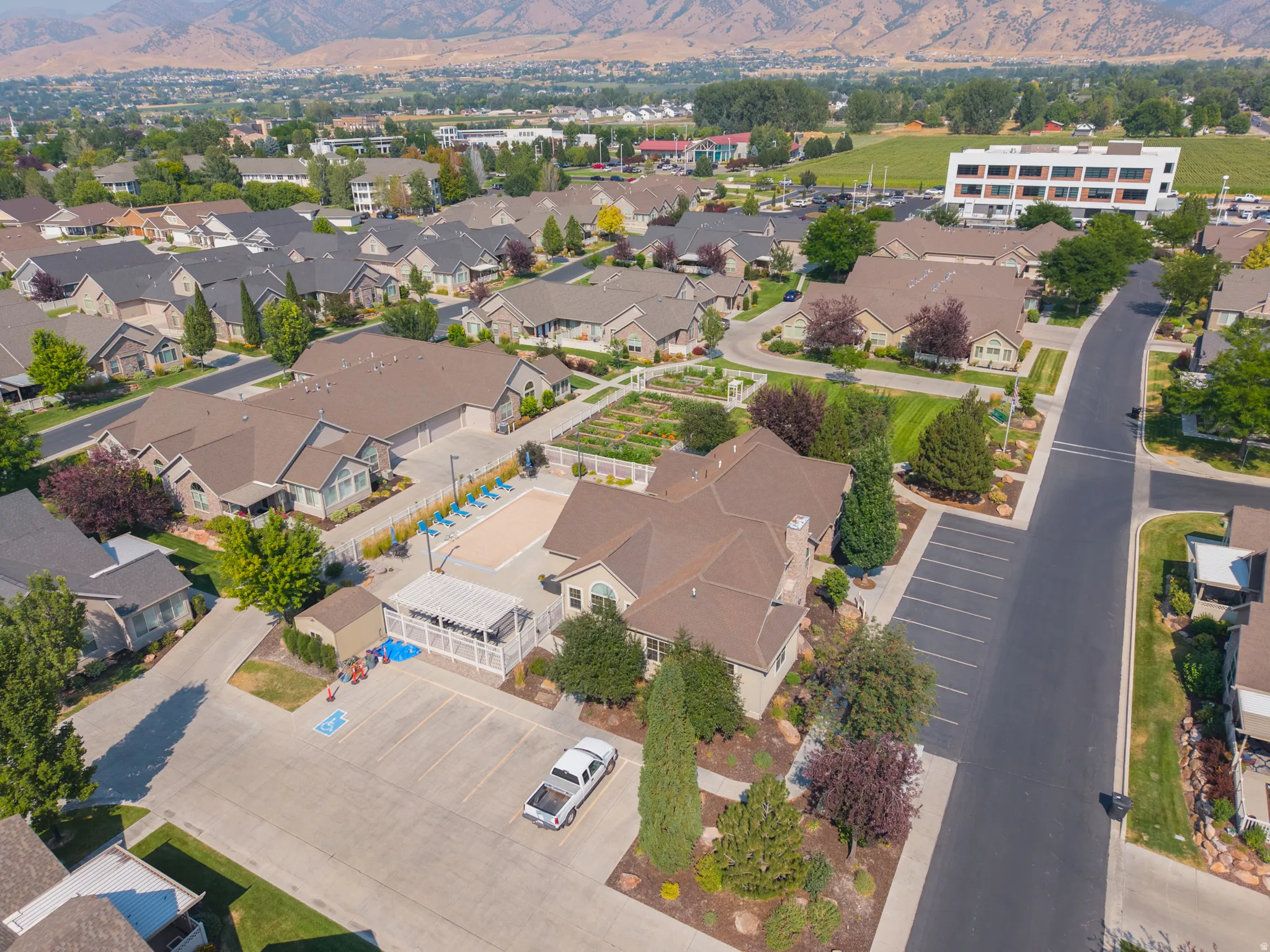 Community pool with surrounding patio, covered outdoor seating area, and adjacent garden plots