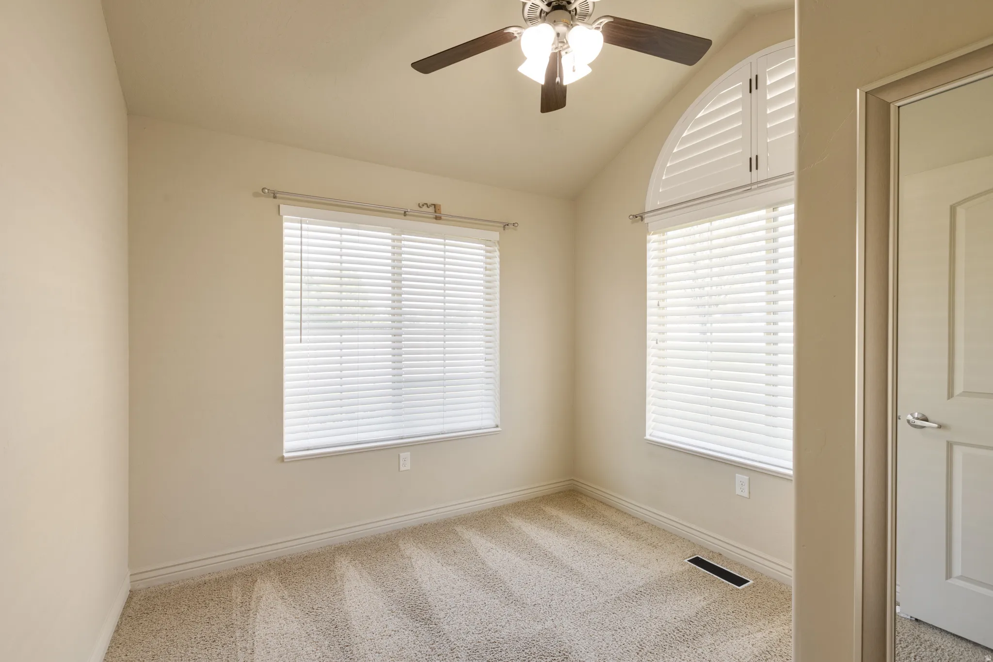 Vaulted ceiling with a ceiling fan, arched window with plantation shutters, additional window with blinds, and light-colored carpet flooring
