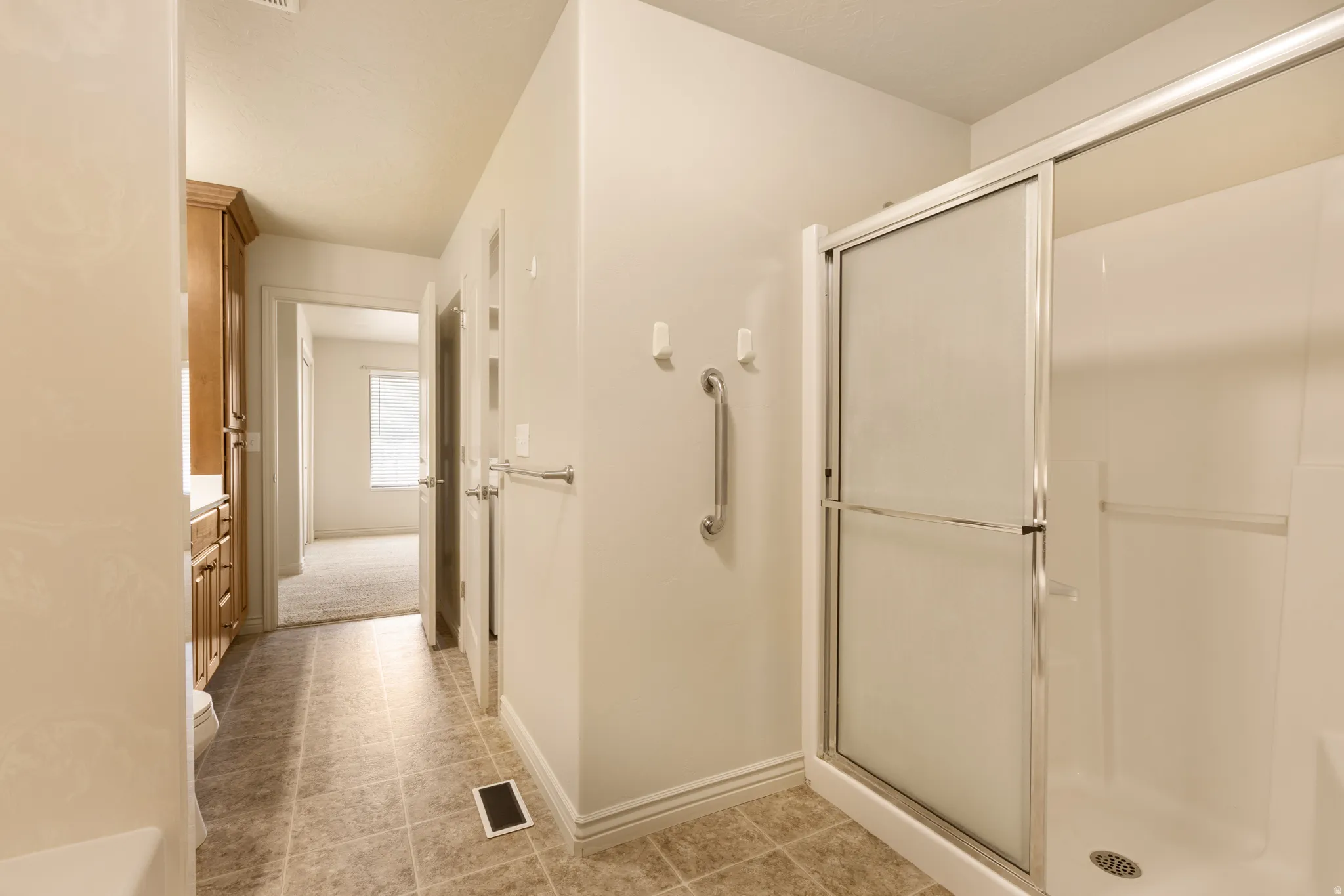 Shower with sliding glass enclosure, white acrylic shower surround, and safety grab bar