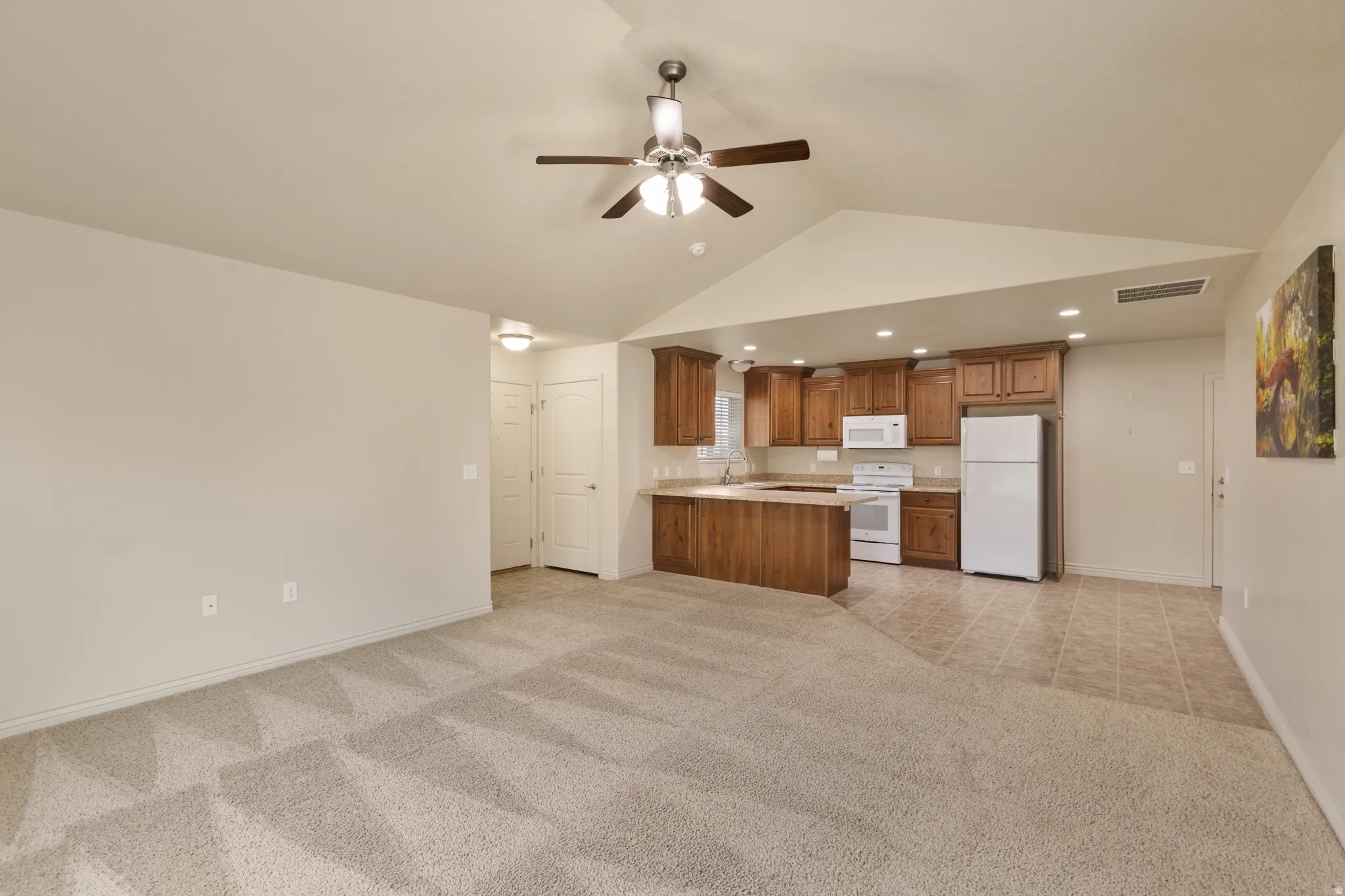Vaulted ceiling with ceiling fan, recessed lighting, wood-finish cabinetry, white appliances, and a breakfast bar