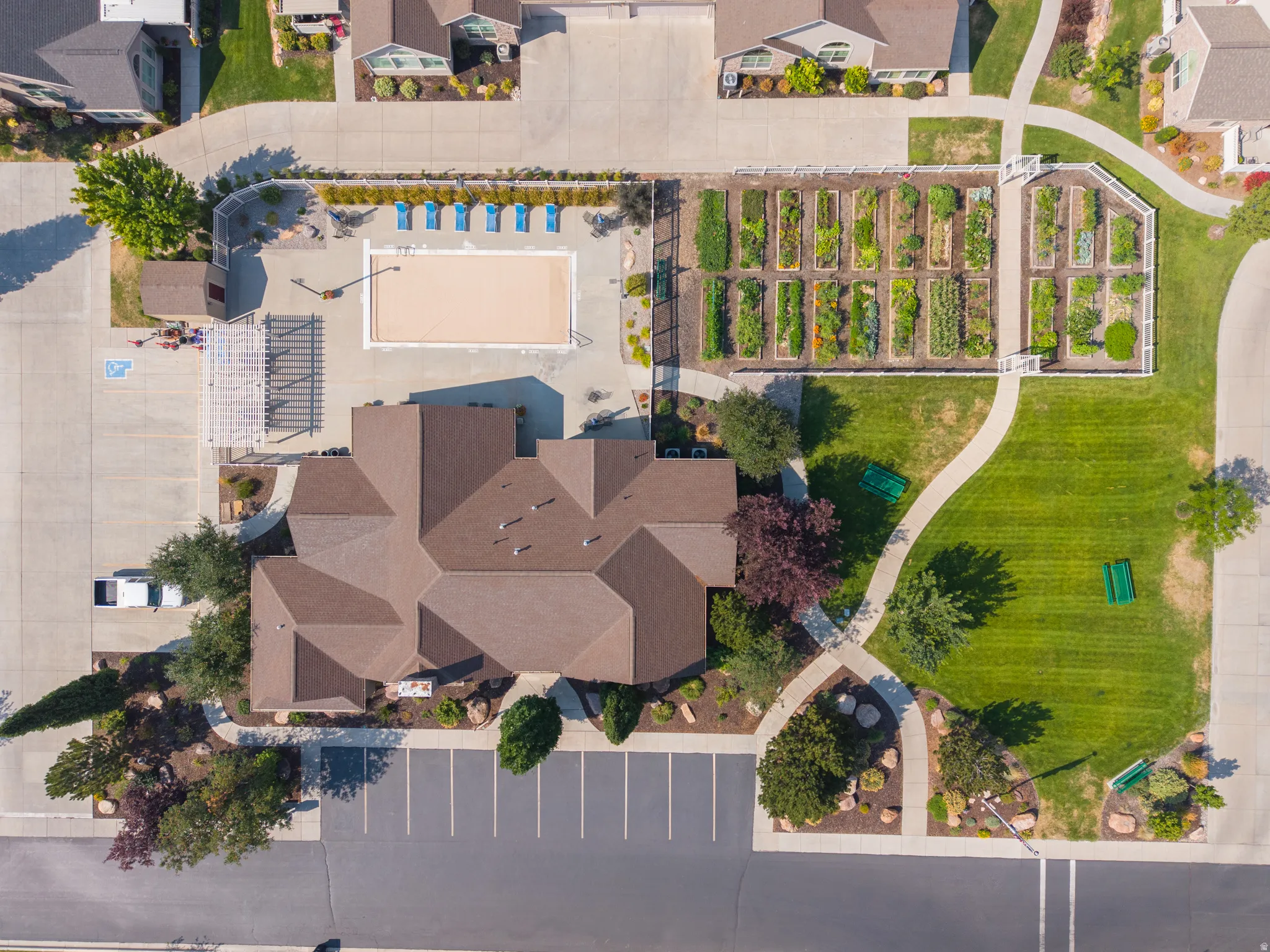 Community building with a shingled roof, a swimming pool, and an adjacent garden area with planted beds