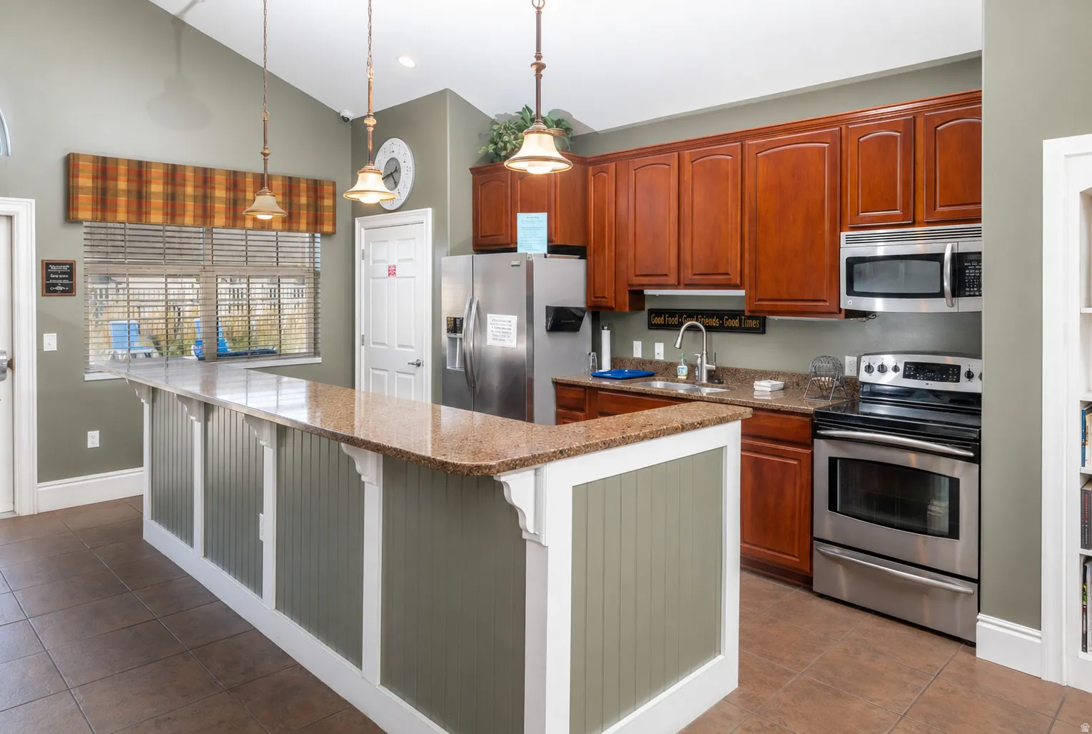 Kitchen featuring an extended island with a stone-finish countertop, wood-finish cabinetry, stainless steel appliances, and tile flooring