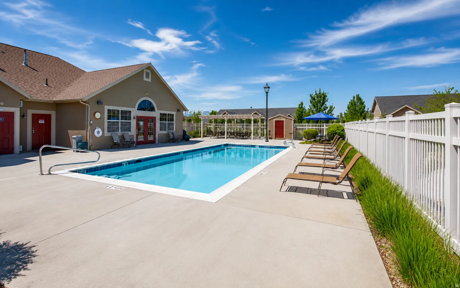 Outdoor swimming pool with concrete decking, a white privacy fence, and a building with red doors