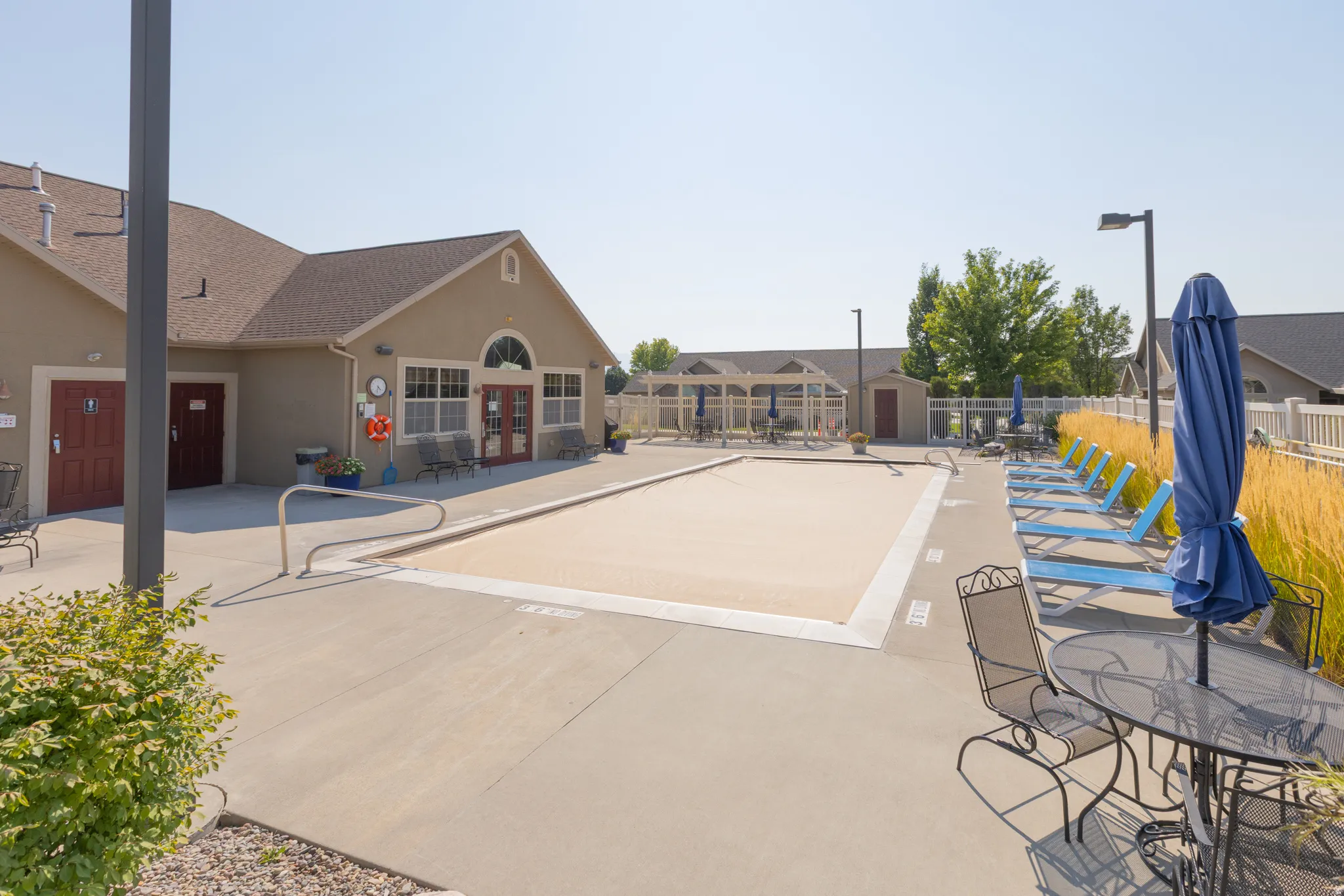 Expansive concrete pool deck with a covered swimming pool, adjacent building with multiple entryways, and decorative fencing