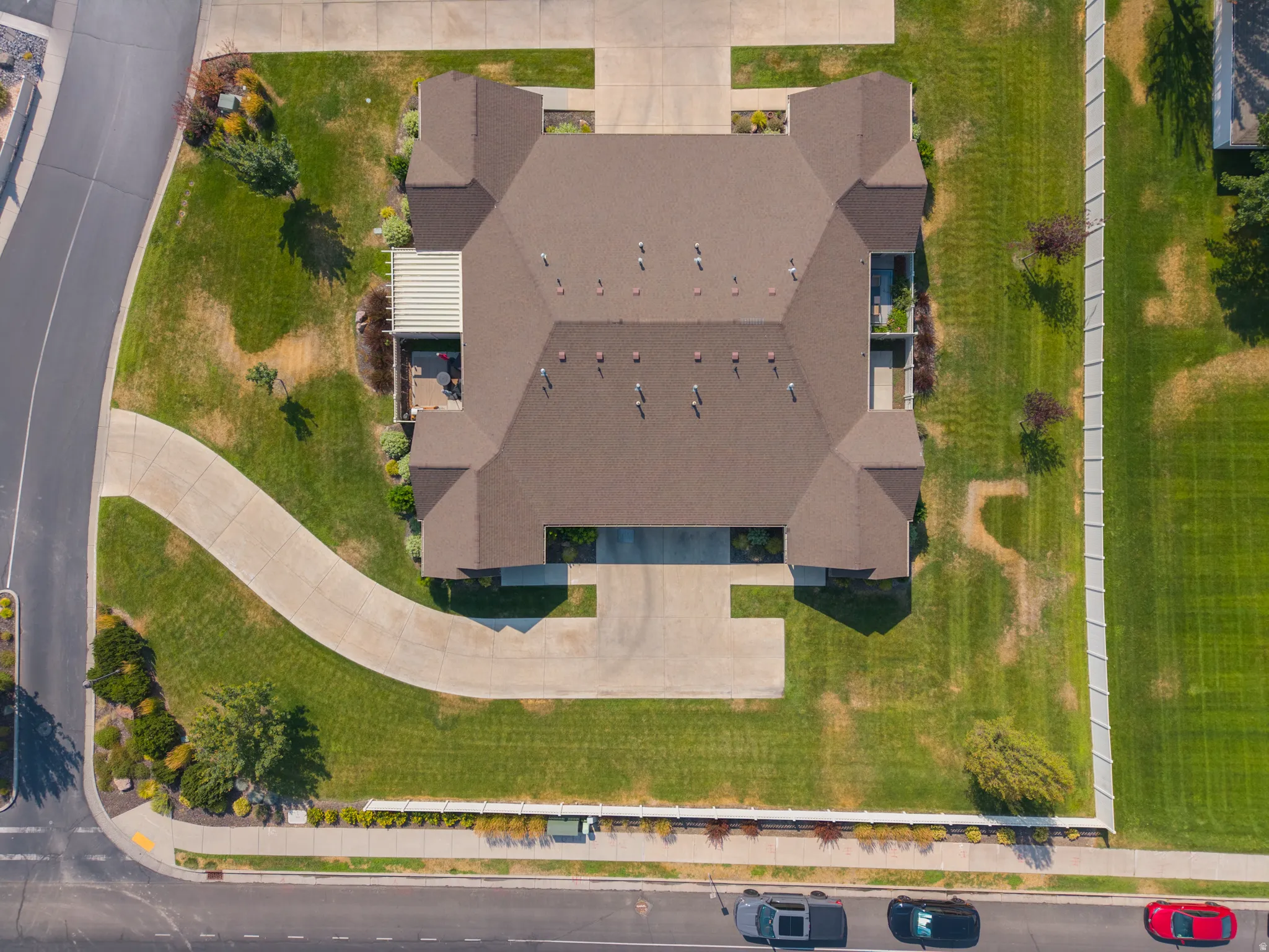 Brown shingle roof with multiple gables, extensive concrete driveway, and a white privacy fence