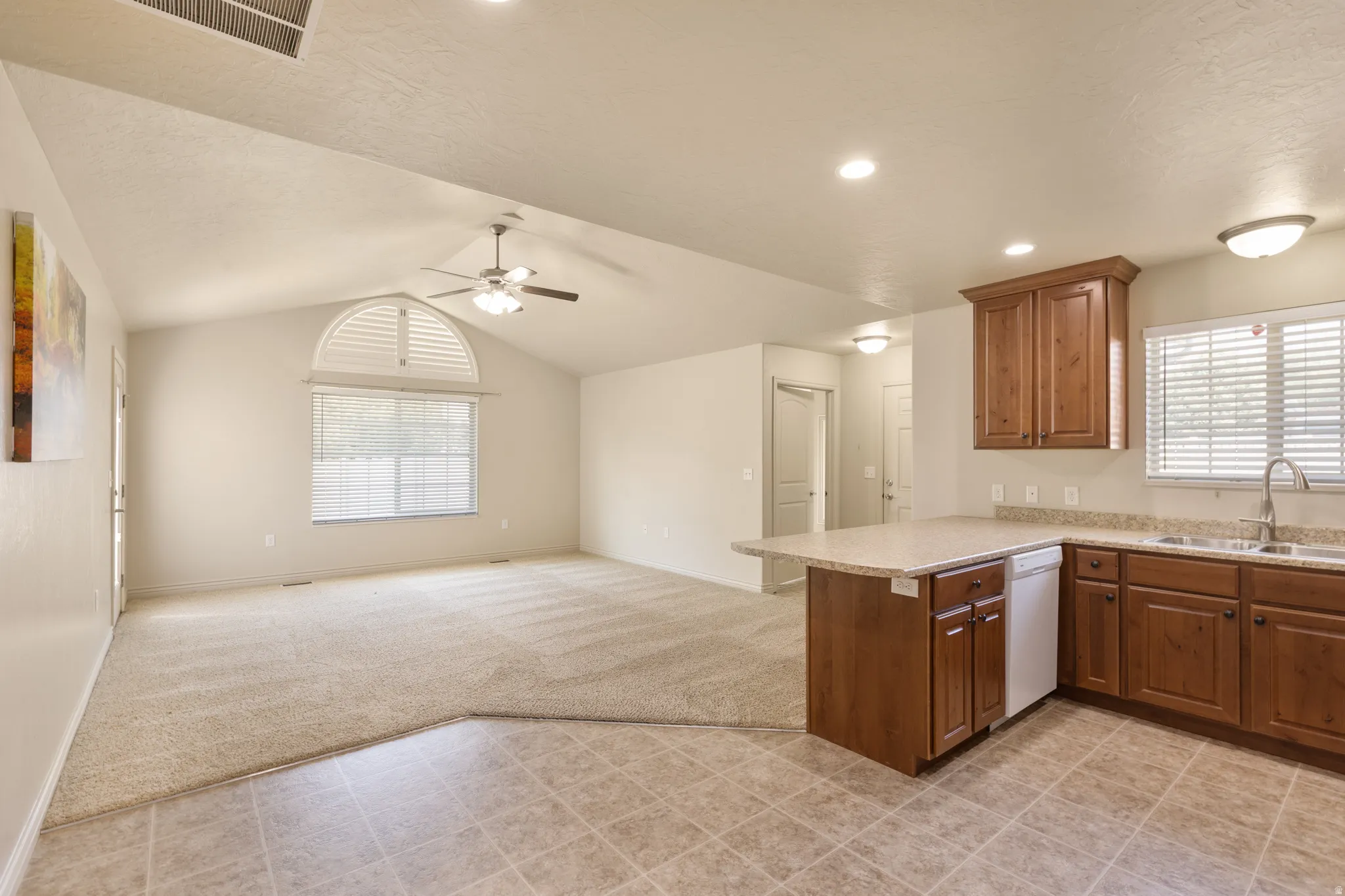 Vaulted ceiling with ceiling fan, arched window with louvered shutters, wood cabinetry, granite-look countertops, and tile flooring
