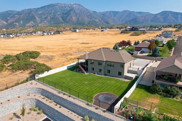 Expansive green lawn, multi-level home exterior, concrete patio, mature landscaping, and mountain backdrop