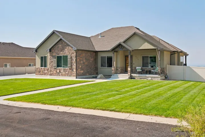 Stone and stucco exterior, covered front porch, asphalt shingle roof, concrete walkway, and a manicured lawn