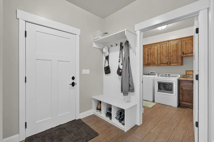 Built-in white storage bench with upper shelving, wood-finish flooring, white panel door, and laundry area with wood cabinetry and countertop