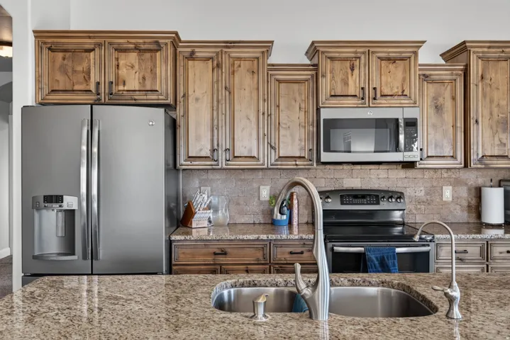 Kitchen featuring light wood-finish cabinetry, stainless steel appliances, a tiled backsplash, and granite countertops