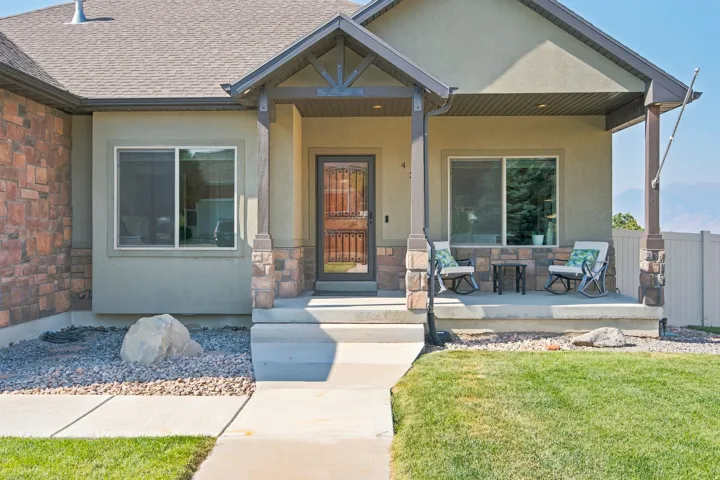 Stucco exterior with stone accents, covered front porch, concrete pathway, and a well-maintained lawn
