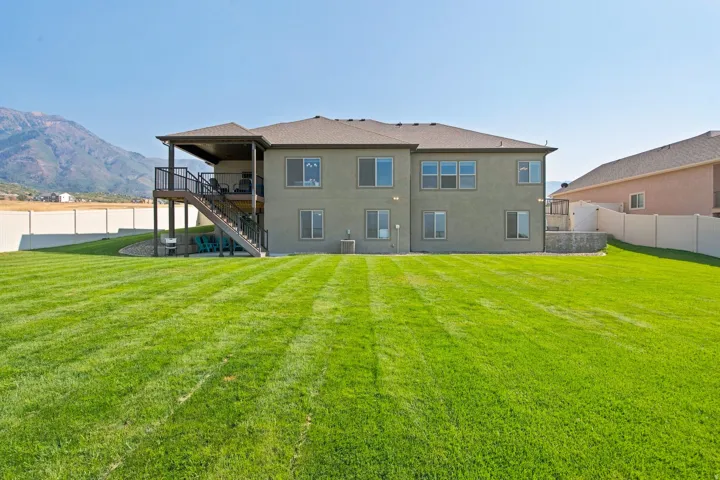Expansive green lawn, two-story residence with a covered deck, and a multi-level retaining wall