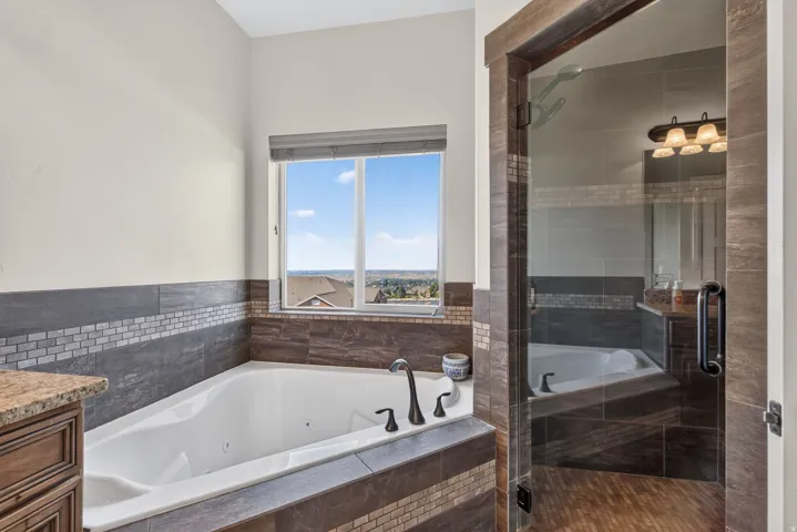 Jetted soaking tub with dark bronze fixtures, tile surround, and an adjacent glass-enclosed shower with wood-finish flooring