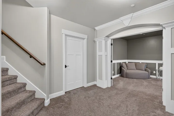 Carpeted staircase with a wood handrail, leading to a plush carpeted area featuring a recessed alcove with decorative archway and wainscoting