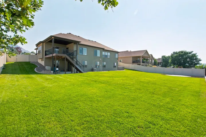 Expansive grassy yard with a two-story residence featuring a covered upper deck and a lower-level patio