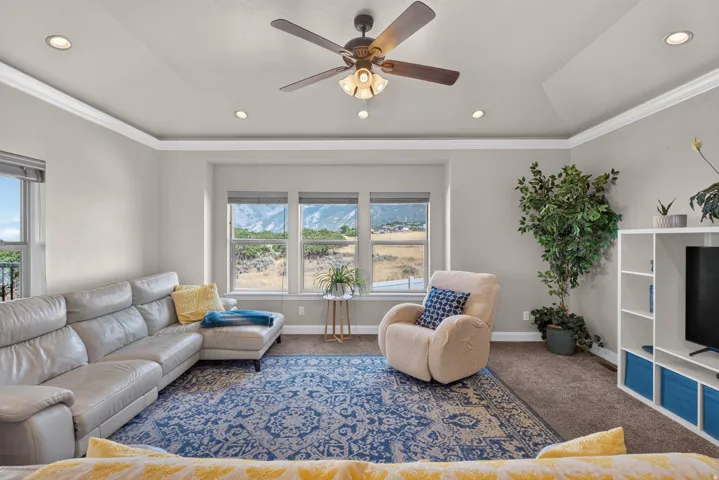 Tray ceiling with crown molding, recessed lighting, ceiling fan, multiple windows, and built-in shelving
