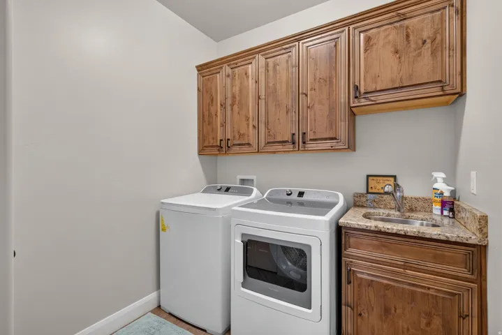 Upper wood cabinetry, lower wood cabinetry, and a utility sink with a granite countertop