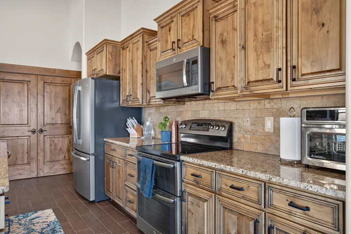 Wood-finish cabinetry with dark hardware, stainless steel appliances, stone tile backsplash, and wood-finish flooring