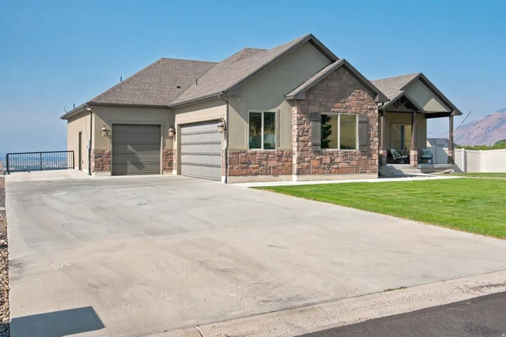 Stucco and stone exterior with a covered porch, attached two-car garage, and a concrete driveway