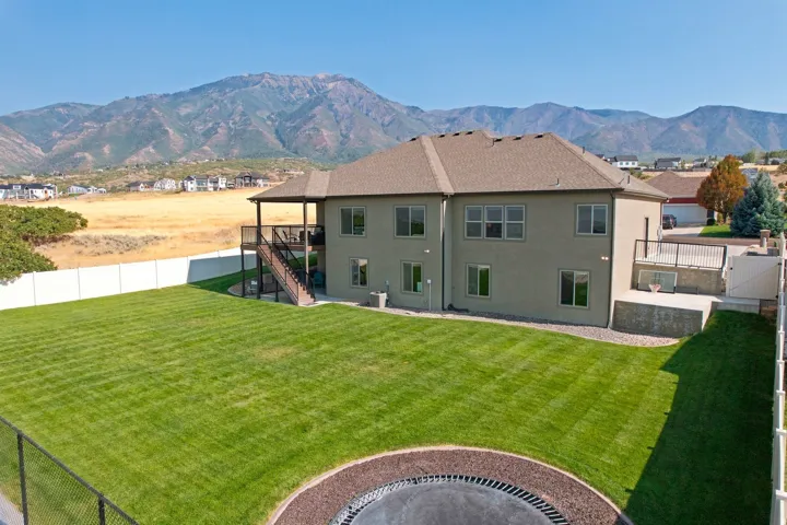 Expansive backyard featuring a manicured lawn, a large upper-level deck, a fenced perimeter, and a patio with a retaining wall