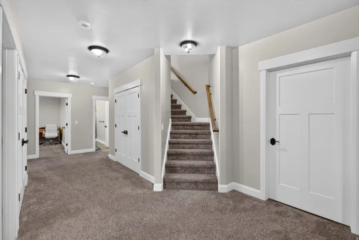 Carpeted flooring extending throughout, staircase with wood handrail, paneled doors with black hardware, recessed wall alcoves, and flush-mount lighting fixtures