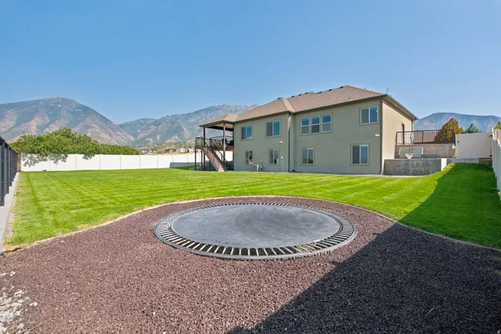 Expansive backyard featuring a manicured lawn, an in-ground trampoline, and a multi-level deck with stairs