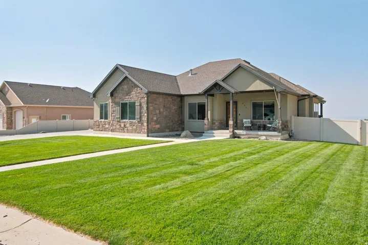 Stucco and stone exterior with covered porch, front patio, and a manicured lawn