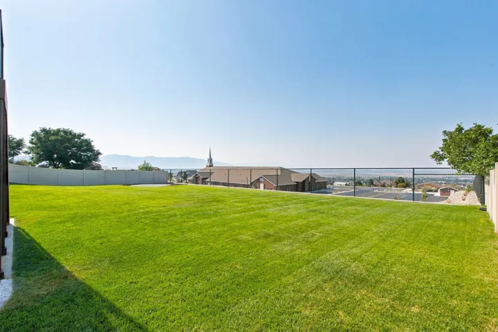 Expansive manicured lawn with a black metal fence, bordered by a concrete retaining wall and white gravel
