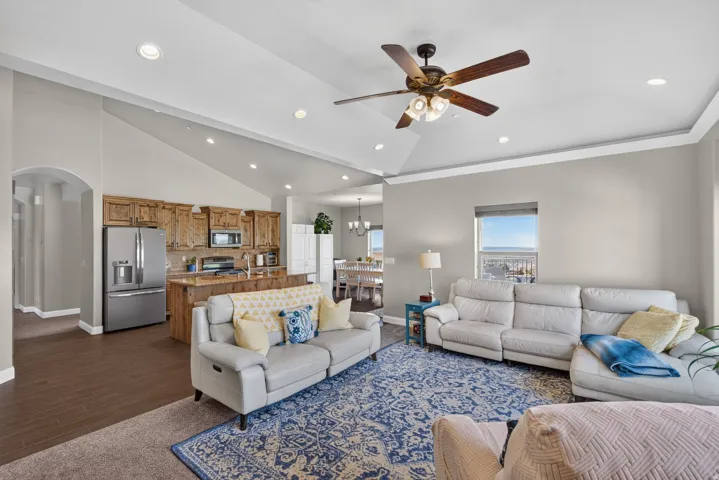 Vaulted ceiling with recessed lighting and a ceiling fan, kitchen featuring wood cabinetry and stainless steel appliances, and wood-finish flooring