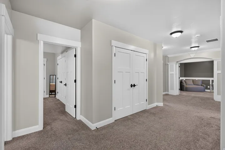 Carpeted hallway with white trim, interior doors with black hardware, and an arched entryway