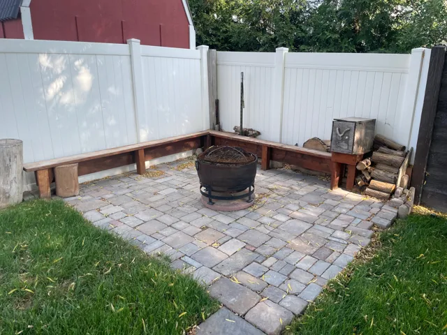 Paver patio featuring a built-in fire pit, perimeter wood benches, and a vinyl privacy fence