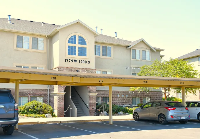 Carport parking with numbered spaces, stucco exterior, brick accents, arched window, and mature landscaping