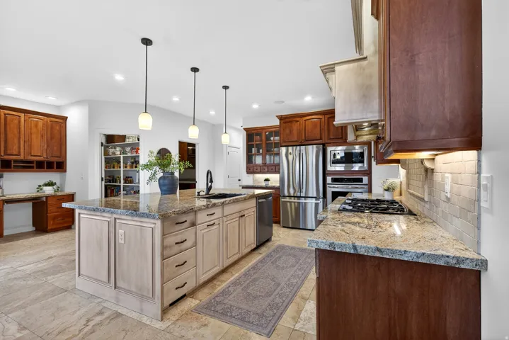 Gourmet kitchen with stainless steel appliances, a center island featuring a sink and pendant lighting, granite countertops, and extensive wood cabinetry