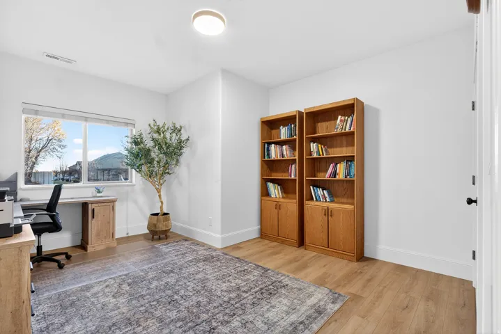 Wood-finish flooring, recessed ceiling light, two built-in wooden bookshelves with cabinet storage, and a large window
