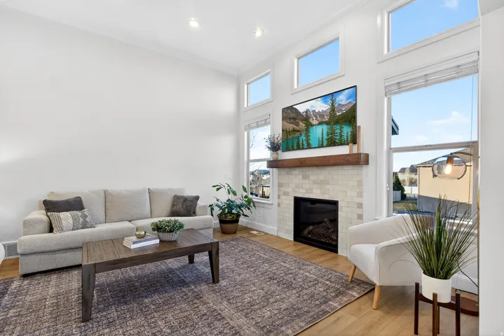 Vaulted ceilings with recessed lighting, wood-finish flooring, a fireplace featuring a tiled surround and wood mantel, and tall windows providing ample light