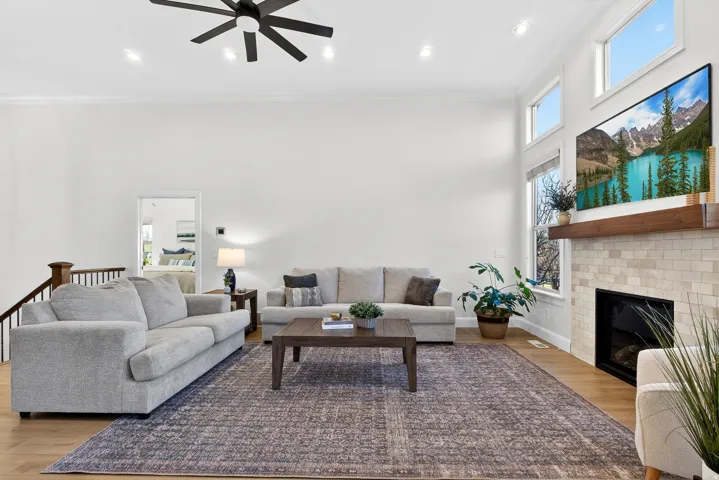 Vaulted ceilings with recessed lighting, wood-finish flooring, a contemporary ceiling fan, and a fireplace with a light-toned tile surround and wood mantel