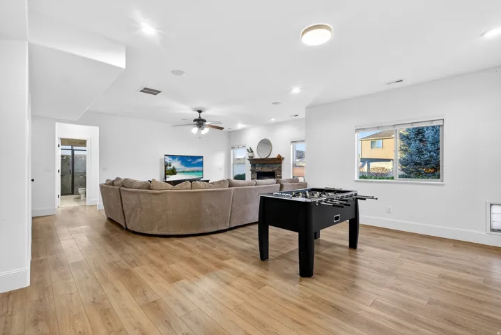 Spacious open-concept room featuring wood-finish flooring, a ceiling fan, recessed lighting, and a fireplace with a stone surround