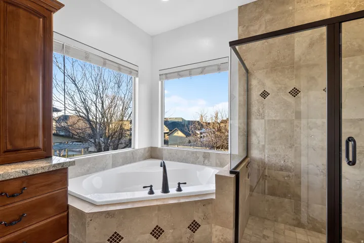 Corner soaking tub with dark bronze fixtures, integrated tile surround, and two expansive windows