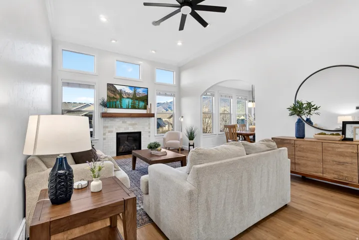 Vaulted ceiling with a ceiling fan, fireplace with a tile surround and wood mantel, wood-finish flooring, recessed lighting, and an arched doorway