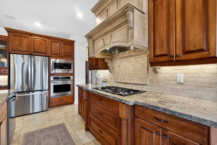 Built-in stainless steel appliances, warm wood cabinetry, granite countertops, tile backsplash, and a gas cooktop