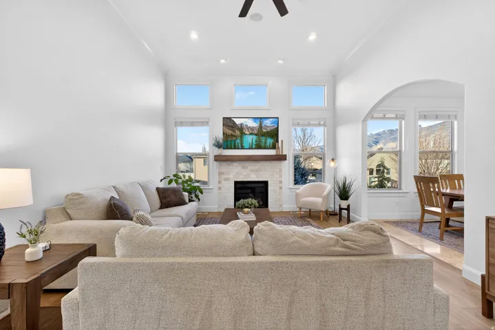 Vaulted ceiling with recessed lighting, fireplace with a wood-finish mantel and tile surround, wood-finish flooring, and an arched doorway