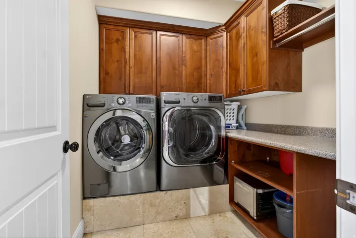Laundry area featuring wood cabinetry, stone-look countertop, and tile flooring