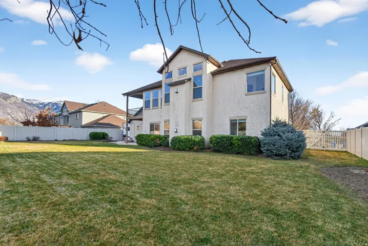 Expansive backyard featuring a manicured lawn, stucco exterior, covered patio, and established perimeter landscaping