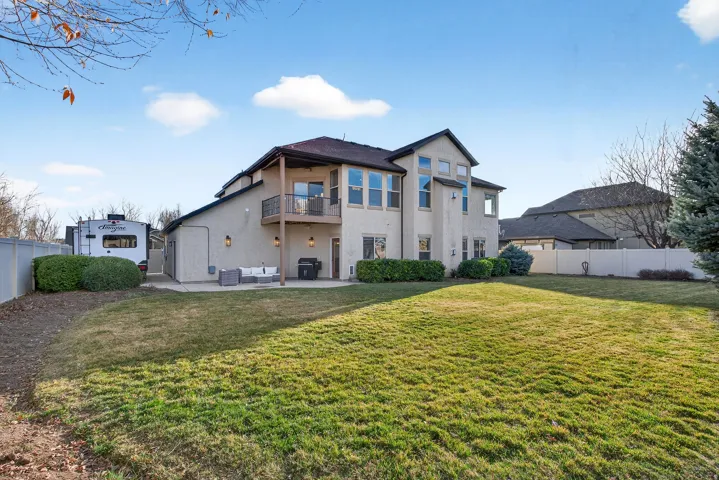 Expansive backyard with a stucco exterior, upper-level balcony with metal railing, ground-level patio, and extensive lawn space