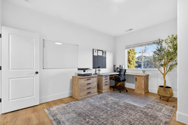 White paneled door with black hardware, wood-finish flooring, white walls, and a large window