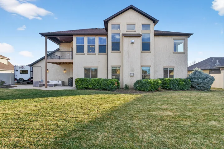 Expansive backyard featuring a concrete patio, covered deck with iron railings, and mature landscaping