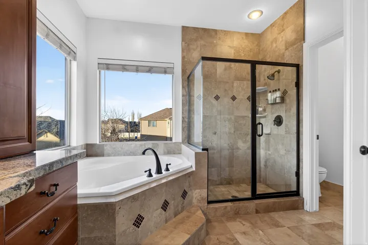 Soaking tub with black fixtures, tiled surround, and large windows