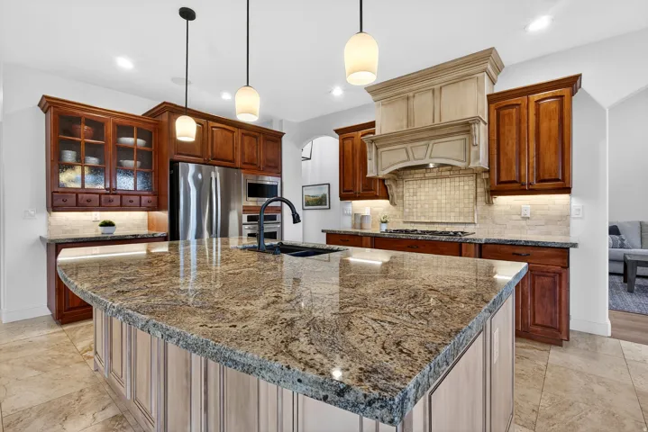 Spacious kitchen featuring an expansive island with a polished countertop, stainless steel appliances, rich wood cabinetry, and recessed lighting